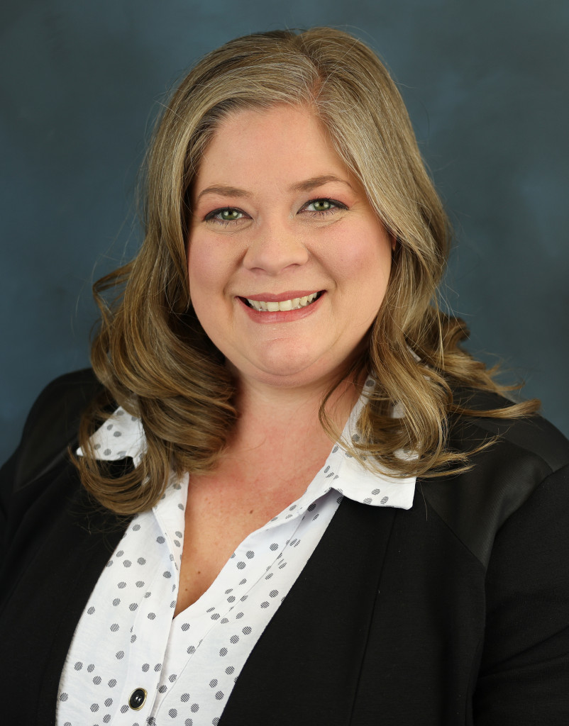 A headshot of Clair McClure who is wearing a white button up shirt with a black blazer.