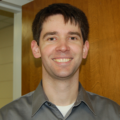 A headshot of BJ Cooley who is wearing a gray button-up shirt.