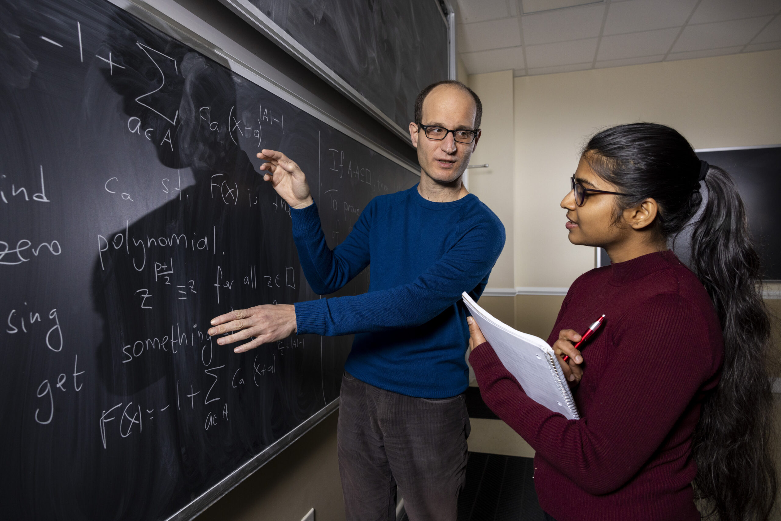An instructor explains information to a student written on a blackboard