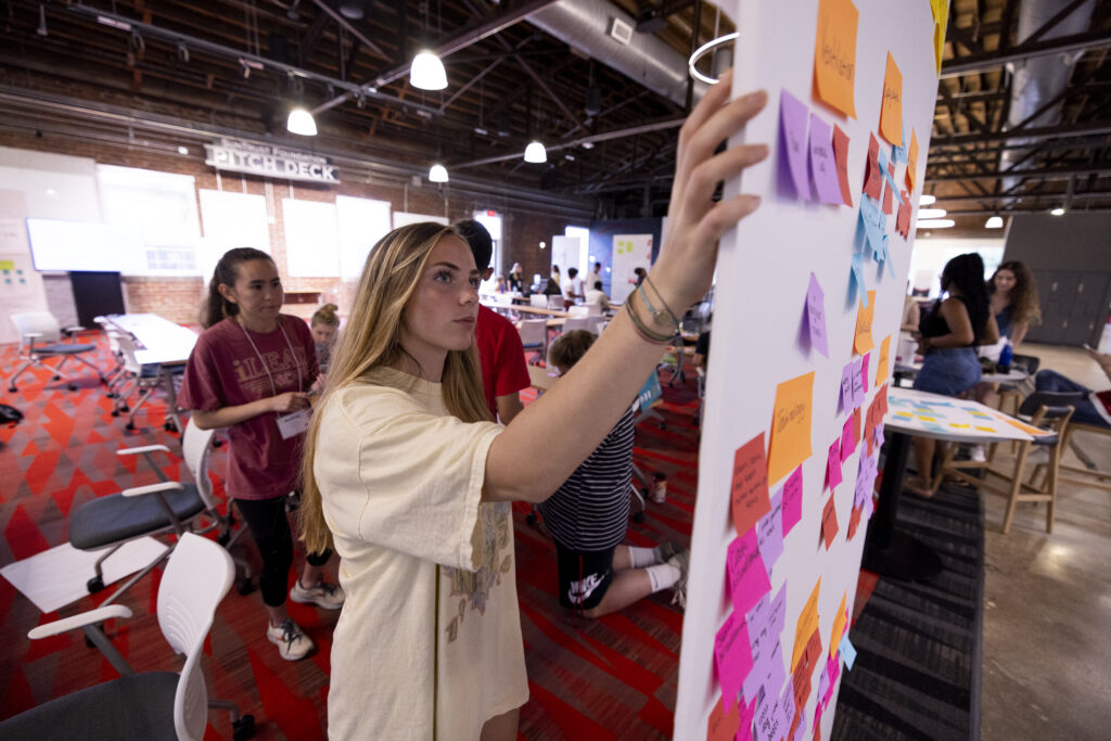 A student presents ideas on a whiteboard with sticky notes
