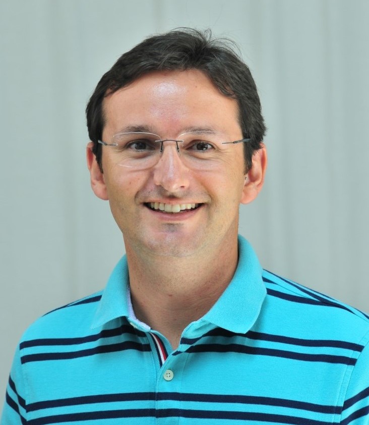 A photo of Rhuanito Ferrarezi, who has short brown hair, glasses, and is wearing a bright teal polo shirt with black stripes.