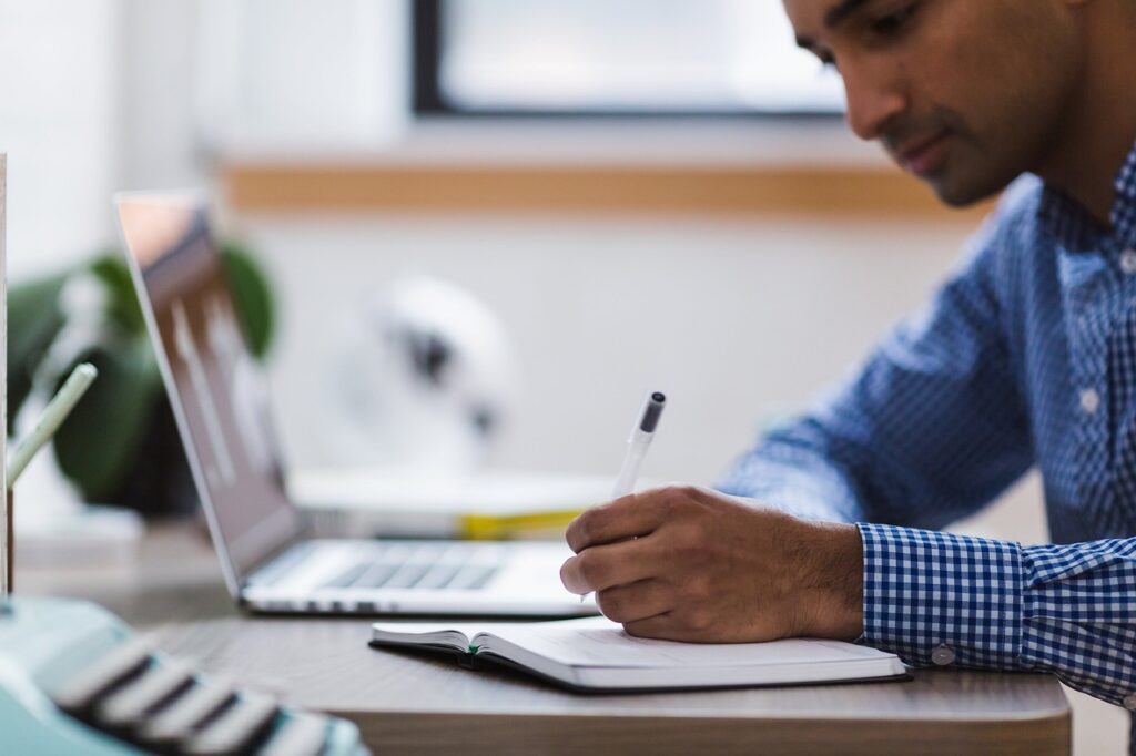 man writing in notebook at desk